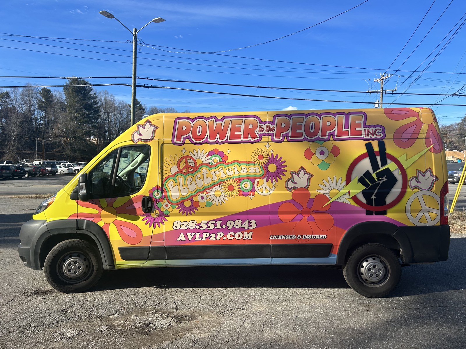 Power to the People's brightly painted electrician van — yellow with peace signs and florals — parked in Asheville